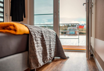 Schlafzimmer auf einem Hausboot am Bärwalder See, graue Decke, gelbe Decke und geöffnete Tür zur Terrasse.
