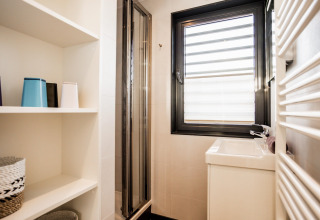 Baño moderno y luminoso en una casa flotante con ducha, ventana grande, lavabo y estanterías.