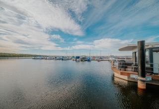 Houseboat at Bärwalder See, Germany, featuring boats docked at the pier under a wide blue sky.