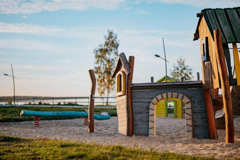 Parque infantil junto a Houseboat am Bärwalder See, con estructuras de madera y balancín junto al lago.