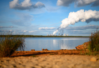 View from Houseboat am Bärwalder See showing power plant smoke rising above a tranquil lake and sky.