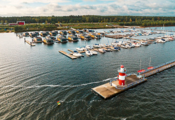 Hausboote am Bärwalder See, Segelboote im Yachthafen, roter Leuchtturm und bewaldete Landschaft.