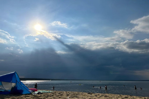 Raggi di sole su Bärwalder See, persone che nuotano e tenda su spiaggia sabbiosa viste dalla Houseboat.