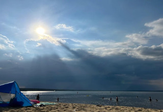 Sunbeams over Bärwalder See, people swimming and a tent on sandy beach, viewed from the Houseboat.
