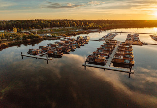 Sunset view of Houseboat am Bärwalder See, featuring houseboats moored on calm water by a forested shore.