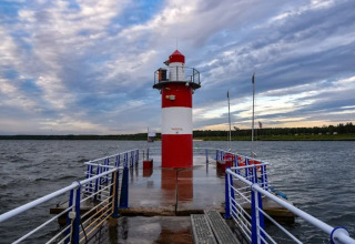 Et billede af en rød og hvid fyrtårn på en mole ved Houseboat am Bärwalder See under en dramatisk himmel.