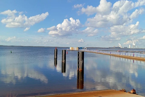 Udsigt fra Houseboat am Bärwalder See med sø, bøjer, en træbro og skyer spejlet i vandet.
