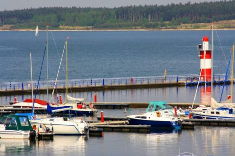 Boats docked in a marina with a red and white lighthouse at Houseboat am Bärwalder See in Germany.