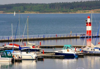 Barcos atracados en un puerto con un faro rojo y blanco en Houseboat am Bärwalder See en Alemania.