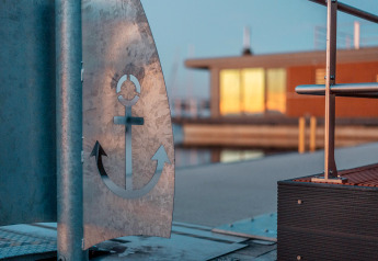 Detailaufnahme eines Ankersymbols aus Metall bei Houseboat am Bärwalder See mit Hausboot im Hintergrund.
