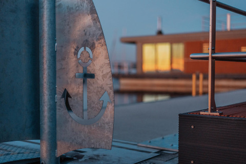 Close-up of anchor design on metal at Houseboat am Bärwalder See with houseboat and sunset in the background.