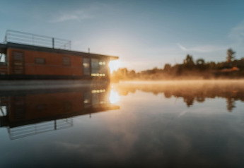 Solopgang over husbåden «am Bärwalder See» i Tyskland, spejlet i det rolige vand.