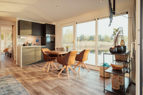 Modern houseboat-interieur aan het Gräbendorfer See met eetruimte, keuken en ramen met zicht op het meer.
