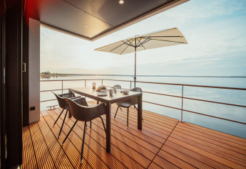 Moderne woonbootterras aan Gräbendorfer See met tafel, stoelen, parasol en prachtig zicht op het meer.