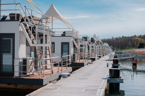 Række af moderne husbåde ved en dock på Gräbendorfer See, omgivet af roligt vand og skov.