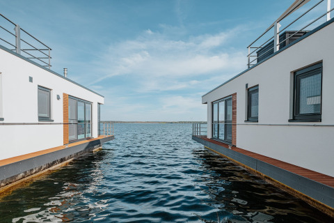 Moderne husbåde på Gräbendorfer See, med blå himmel og fredeligt vand imellem boligerne.