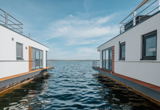 Casa flotante moderna en Gräbendorfer See, cielo azul y agua serena entre dos viviendas sobre el lago.