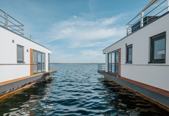 Moderne husbåde på Gräbendorfer See, med blå himmel og fredeligt vand imellem boligerne.