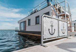 Houseboat sul Gräbendorfer See con ringhiere moderne a tema ancora e acque tranquille circostanti.