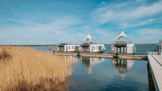 Husbåde ved Houseboat am Gräbendorfer See under blå himmel, omgivet af siv og roligt vand.