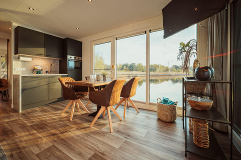 Modern huisbootinterieur met eethoek, keuken en ruime ramen die uitkijken op het Gräbendorfer See.