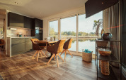 Modern huisbootinterieur met eethoek, keuken en ruime ramen die uitkijken op het Gräbendorfer See.