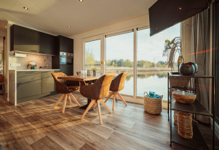 Modern huisbootinterieur met eethoek, keuken en ruime ramen die uitkijken op het Gräbendorfer See.