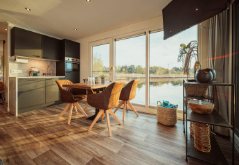 Intérieur moderne de péniche avec salle à manger, cuisine et grandes fenêtres sur le lac Gräbendorfer See.