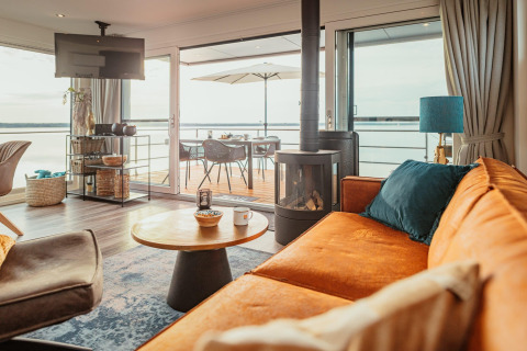 Salón moderno y luminoso en Houseboat am Gräbendorfer See con acceso a terraza y vistas al lago a través de puertas.