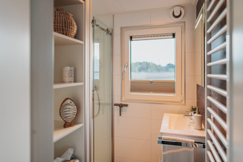 Moderne badkamer op een woonboot aan het Gräbendorfer See met douche, raam en open planken.