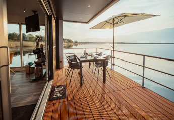 Terrazza moderna di houseboat sul Gräbendorfer See con tavolo, sedie, ombrellone e vista lago.