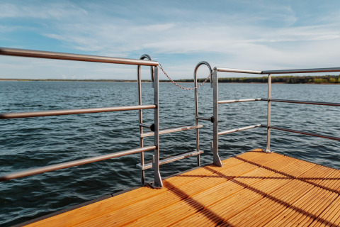 Vista dalla terrazza della Houseboat am Gräbendorfer See con pavimento in legno e cancello metallico sul lago.