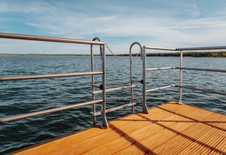 Udsigt fra terrasse på Houseboat am Gräbendorfer See med trædæk og metallåge over søen en solrig dag.
