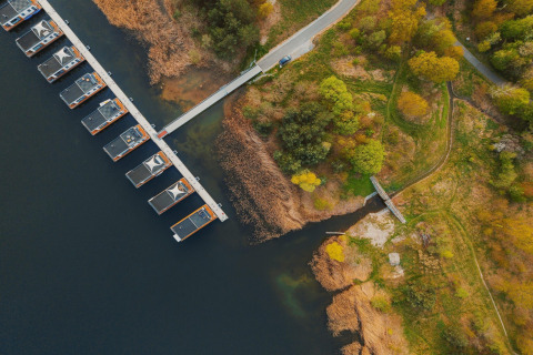 Luftfoto af husbåde ved Houseboat «am Gräbendorfer See» med bro og omgivende grønt område i Tyskland.