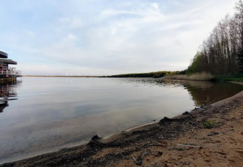 View of Gräbendorfer See from sandy shore with houseboat on the left and forest on the right.