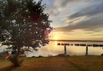 Sonnenuntergang über dem Gräbendorfer See von einem Hausboot aus, mit Baum und ruhigem Wasser.