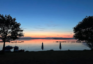View from Houseboat am Gräbendorfer See overlooking the lake at sunset, boats and umbrellas visible.