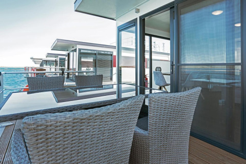 Moderne terras op woonboot Floating 33 met zeezicht, glazen tafel en gevlochten stoelen om te ontspannen.
