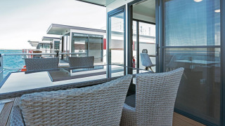 Modern terrasse på husbåd Floating 33 med havudsigt, glasbord og flettede stole til afslapning.