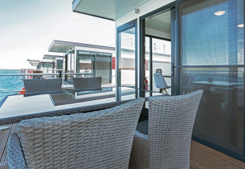 Moderne Terrasse auf Hausboot Floating 33 mit Meerblick, Glastisch und geflochtenen Stühlen.
