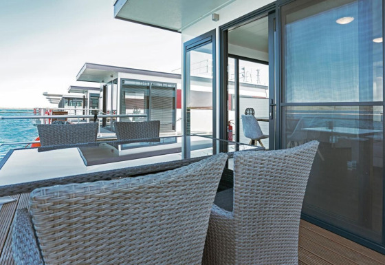 Moderne terras op woonboot Floating 33 met zeezicht, glazen tafel en gevlochten stoelen om te ontspannen.