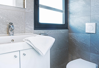 Modern bathroom on houseboat with white sink, towel, chrome faucet, window and grey tiled walls in Germany.