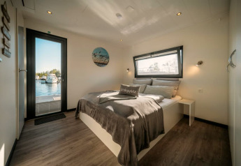 Helles Schlafzimmer auf einem Hausboot in Zehdenick mit Doppelbett, Fenster und Blick aufs Wasser.
