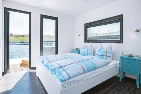 Bedroom on the houseboat 'Floating 33 - LP 16' in Germany, featuring blue bedding, modern decor, and water views.