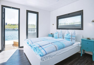 Bedroom on the houseboat 'Floating 33 - LP 16' in Germany, featuring blue bedding, modern decor, and water views.