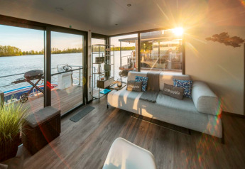 Solrig stue på husbåd i Zehdenick med moderne sofa, søudsigt og udgang til terrasse over vandet.