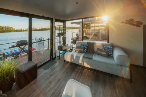Sunny living room on a houseboat in Zehdenick with modern sofa, lake view, and access to a terrace.