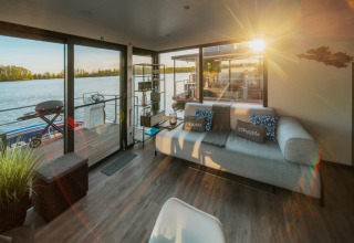Soggiorno soleggiato su una houseboat a Zehdenick con divano moderno, vista lago e terrazza.