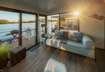 Salon ensoleillé sur une péniche à Zehdenick avec canapé, vue sur le lac et accès à la terrasse.