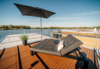 Solrig tagterrasse på husbåd i Zehdenick med moderne solseng, sort parasol og smuk udsigt over vandet.